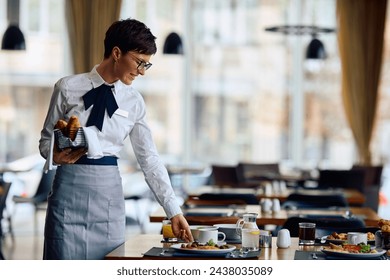 Happy hotel waitress serving breakfast at the tables in a restaurant. Copy space.  - Powered by Shutterstock