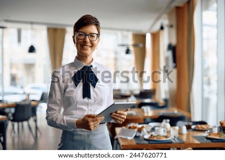 Happy hotel waitress using digital tablet in a restaurant and looking at camera. Copy space.