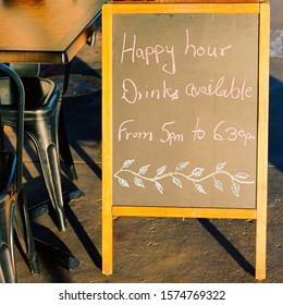 Happy Hour Drinks Chalkboard Sign Outside A City Restaurant, Bright From Afternoon Sunlight