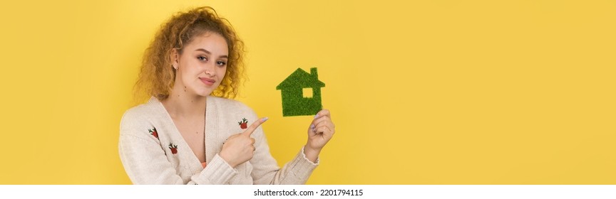 Happy House Buyer. A Young Girl Holds A Model Of A Green House In Her Hands. The Concept Of Green Energy, Ecology.