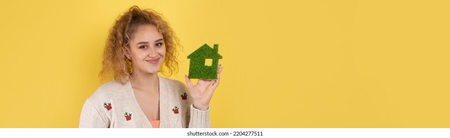 Happy House Buyer. A Young Girl Holds A Model Of A Green House In Her Hands. The Concept Of Green Energy, Ecology.