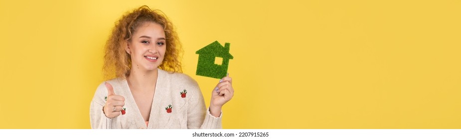 Happy House Buyer. A Young Girl Holds A Model Of A Green House In Her Hands. The Concept Of Green Energy, Ecology.