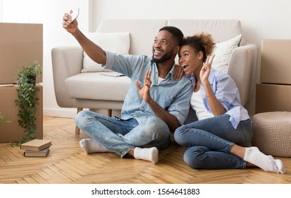 Happy House Owners. Afro Couple Taking Selfie With Smartphone Gesturing Victory Sign After Moving Into New Home. Copy Space - Powered by Shutterstock