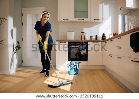Happy housemaid using mop while sweeping floor in the kitchen. Copy space. 