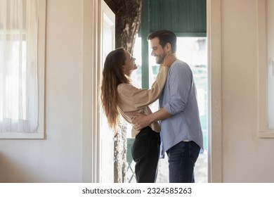 Happy houseowners. Affectionate loving young woman wife hugging embracing smiling millennial man husband lover spouse meeting or seeing off at the door of new rented purchased house apartment dwelling
