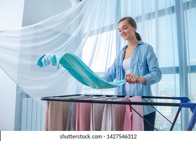 Happy housewife hangs wet linen on the clothes dryer after laundry at home. Household chores and housekeeping 