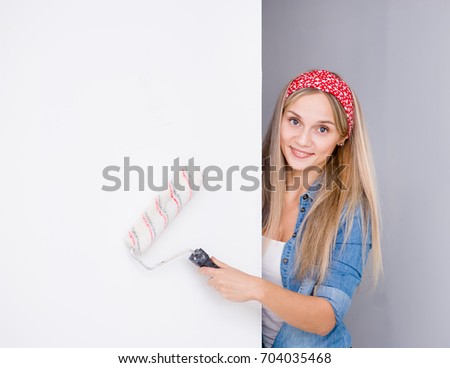 Happy housewife looks above white banner with paint roller. Space for text