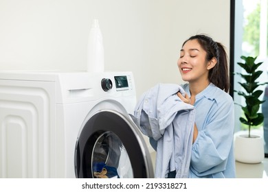 Happy housewife opens the front of the washing machine and smiles to receive the laundry that has been washed at house. Woman smelling fragrant clean clothes washed from softener and washing machine.