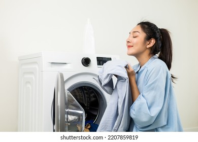 Happy housewife opens the front of the washing machine and smiles to receive the laundry that has been washed at house. Woman smelling fragrant clean clothes washed from softener and washing machine. - Shutterstock ID 2207859819