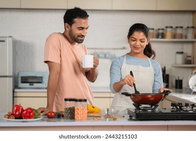 happy husband with coffee spending time with cooking wife at kitchen - concept of relationship bonding, morning routine and family affection. - Powered by Shutterstock