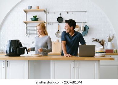 Happy husband remote working or distance learning online from home office while his wife cooking toast bread by Air Fryer machine for breakfast at kitchen table. New normal work lifestyle at home.