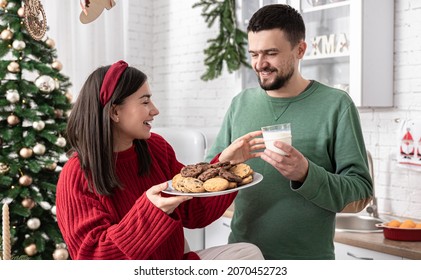 Happy Husband And Wife With Christmas Cookies And Milk In The Kitchen.