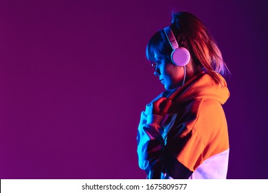Happy igen teen hipster fashion girl model wear stylish glasses headphones enjoy listen new cool trance music mix stand at purple studio background in trendy 80s 90s club party light, profile view - Shutterstock ID 1675809577