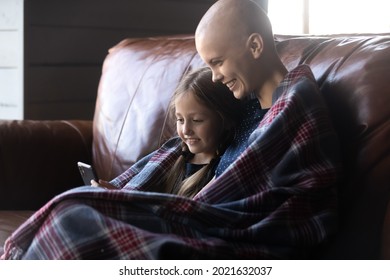 Happy Ill Mom And Daughter Kid Relaxing In Plaid On Sofa, Using Mobile Phone, Making Video Call, Watching Virtual Content, Shopping Online. Mom With Cancer And Child Enjoying Family Time Together