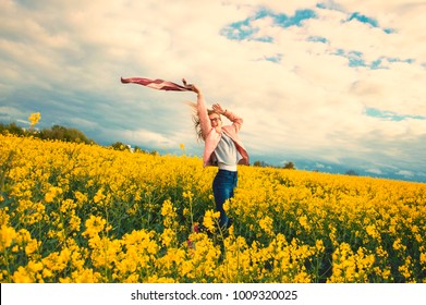 happy independent girl in rapeseed field in windy weather waving a waving scarf