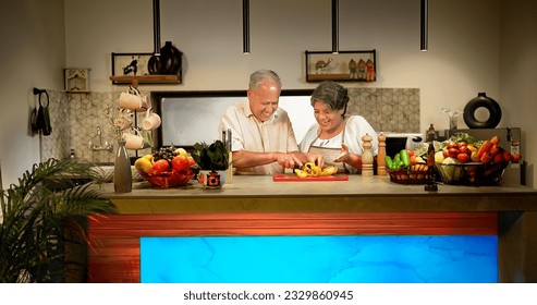 Happy Indian aged couple preparing vegetarian salad standing in modern kitchen at home. Senior wife in apron teaching husband
to cut fresh capsicum slice on chopping board spend time enjoy together - Powered by Shutterstock
