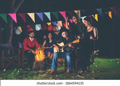 Happy Indian Asian Friends Playing Music And Enjoying Bonfire Or Campfire In Nature