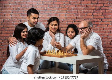 Happy Indian asian multigenerational family of six playing chess or Shatranj which is a popular board game, wearing white cloths against red brick wall - Powered by Shutterstock