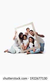 Happy Indian Asian Multigenerational Family Of Six Looking Through An Empty Frame, Standing Or Sitting Against White Background Wearing White Cloths And Blue Denim Jeans