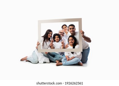 Happy Indian Asian Multigenerational Family Of Six Looking Through An Empty Frame, Standing Or Sitting Against White Background Wearing White Cloths And Blue Denim Jeans