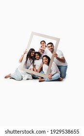 Happy Indian Asian Multigenerational Family Of Six Looking Through An Empty Frame, Standing Or Sitting Against White Background Wearing White Cloths And Blue Denim Jeans