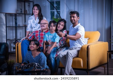 Happy Indian asian multigenerational family watching television or tv while sitting on sofa at home - Powered by Shutterstock