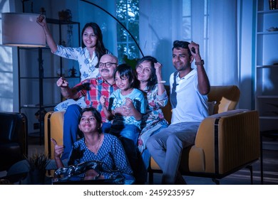Happy Indian asian multigenerational family watching television or tv while sitting on sofa at home - Powered by Shutterstock