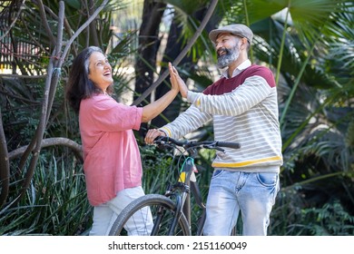 Happy Indian Asian Senior Couple Walking Their Bike Talking In Park.mature Couple In Summer Park.Retired Man And Old Woman With Bicycles Outside Nature.