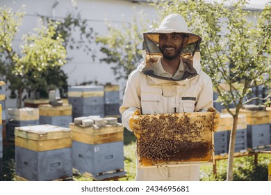 Happy Indian beekeeper takes out a frame with bees and honey from a beehive on a bee farm. The concept of beekeeping - Powered by Shutterstock