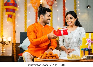 Happy indian brother giving gift or present to sister after tying rakhi at home during raksha bandhan festive celebration - concpet of Sibling Love, Happy Moments and Family Bonding