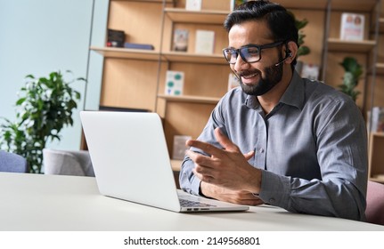 Happy indian business man remote teacher, customer support manager wearing headset talking at virtual meeting consulting client on video call giving distance learning class at home office call center. - Shutterstock ID 2149568801
