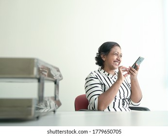 Happy Indian Businesswoman Leave A Voice Message On Her Cellphone. Office Setting.