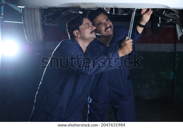 Happy\
Indian car mechanics standing and working together in service\
station. Car specialists examining the lifted car. Professional\
repairmen wearing mechanic uniform in blue\
color.