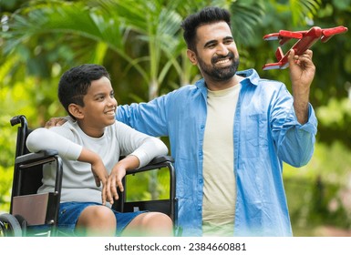 Happy indian caring father showing airplane toy to kid with disability on wheelchair at park - concept of determination, parental support and medical recovery - Powered by Shutterstock