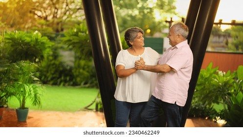 Happy Indian cheerful elderly senior couple enjoy slow romantic dance dating together spend time outdoor home. Overjoyed old mature husband wife smiling holding hand spinning celebrate timeless love - Powered by Shutterstock