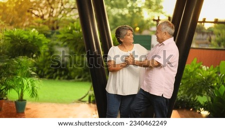Happy Indian cheerful elderly senior couple enjoy slow romantic dance dating together spend time outdoor home. Overjoyed old mature husband wife smiling holding hand spinning celebrate timeless love