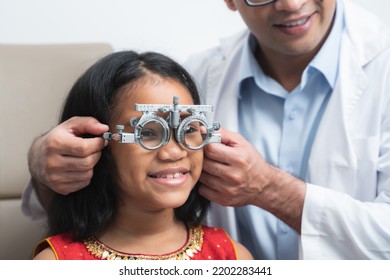 Happy Indian Child Girl Doing Examine Eyesight With Trial Frame And Lens With Ophthalmologist Or Optometrist For Eyes Test At Hospital Or Optometry Clinic