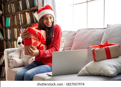 Happy Indian Child Kid Girl Wearing Santa Hat Holding Christmas Gift Box, Showing New Year Present To Webcam Talking With Family, Social Distance Friend By Video Conference Call Meeting Chat At Home.