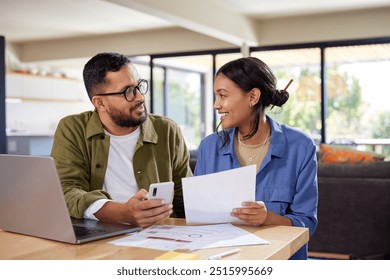 Happy indian couple discussing home finance while holding documents and working on laptop and mobile phone. Middle eastern man and casual woman sitting at table and discussing expenses. - Powered by Shutterstock