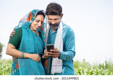 Happy Indian Couple Farmers Using Smartphone Application In Agriculture Field, Rural Man Woman Holding Mobilephone, Male Female Looking At Cellphone Screen,  Digital India Concept.  Online Payment. 