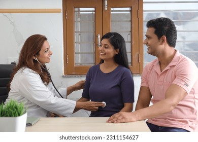 Happy Indian couple getting checkup by gynecologist to make sure that mother is expecting baby. Young woman patient with husband getting checked up by senior gynecologist during consultation. Smiles - Powered by Shutterstock