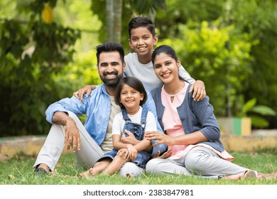 Happy indian couple with kids embracing by looking at camera while sitting at park - concept of relationship, family time and togetherness - Powered by Shutterstock