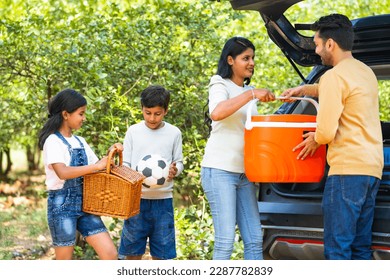 Happy Indian couple with kids taking out bags and picnic bucket from car boot - concept of summer holidays, togetherness and family vacation - Powered by Shutterstock