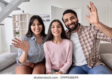 Happy Indian Couple And Teen Child Daughter Waving Hands Looking At Camera Sitting On Couch At Home. Cheerful Family Having Video Call Virtual Meeting Greeting In Online Chat, Webcam View Portrait.