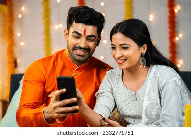 Happy indian couple using mobile phone during festival celebration at home - concept of checking new festive sales, online or ecommerce discounts and social media sharing. - Powered by Shutterstock