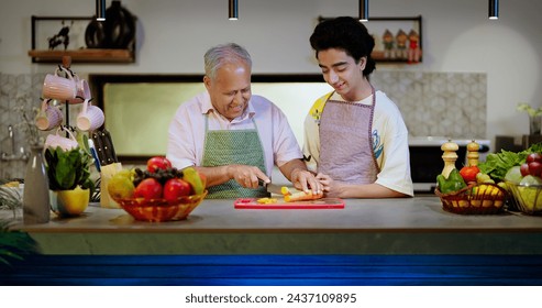 Happy Indian cute teen age boy standing in modern kitchen elder senior grandpa teaching to cut fresh carrot slice on chopping board prepare healthy vegan food salad enjoy learn spend time together - Powered by Shutterstock