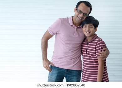 Happy Indian Dad And Son Hugging And Smiling At Camera On White Wall