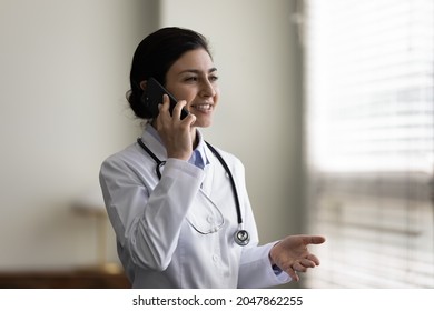 Happy Indian doctor giving telephone consultation, talking to patient on mobile phone, making call from hospital office. General practitioner, therapist, counselor answering questions on hotline