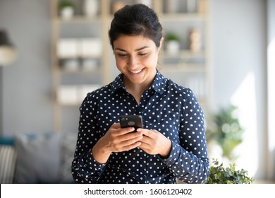 Happy Indian Ethnic Young Woman Using Mobile Apps Holding Smart Phone Playing Games Texting Messages Enjoy Social Media Shopping Applications Search Job Vacations Online In Smartphone At Home Office