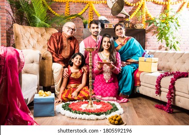 Happy Indian Family Celebrating Ganesh Festival Or Chaturthi - Welcoming Or Performing Pooja And Eating Sweets In Traditional Wear At Home Decorated With Marigold Flowers